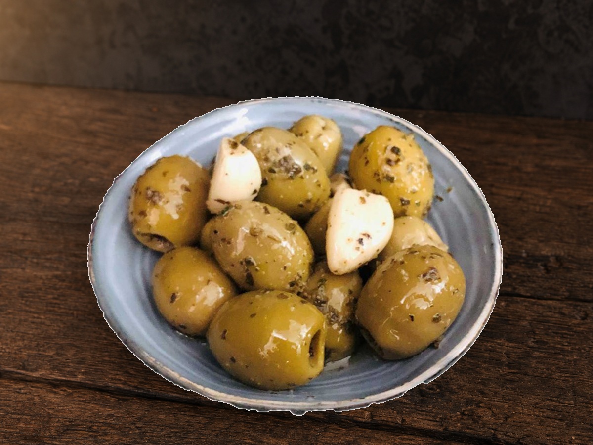 Knoflook olijven met knoflooktenen in een schaaltje op een donkere houten plank