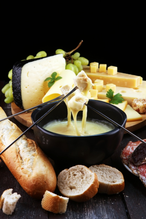 Romige kaasfondue in een zwarte pan met brood en verschillende kazen