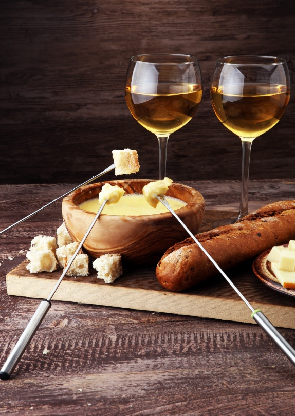 Kaasfondue met brood en twee glazen witte wijn op een houten tafel