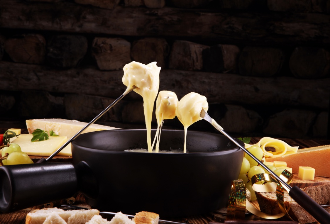 Gesmolten kaas aan fonduevorken boven een zwarte fonduepan, met kaas en brood